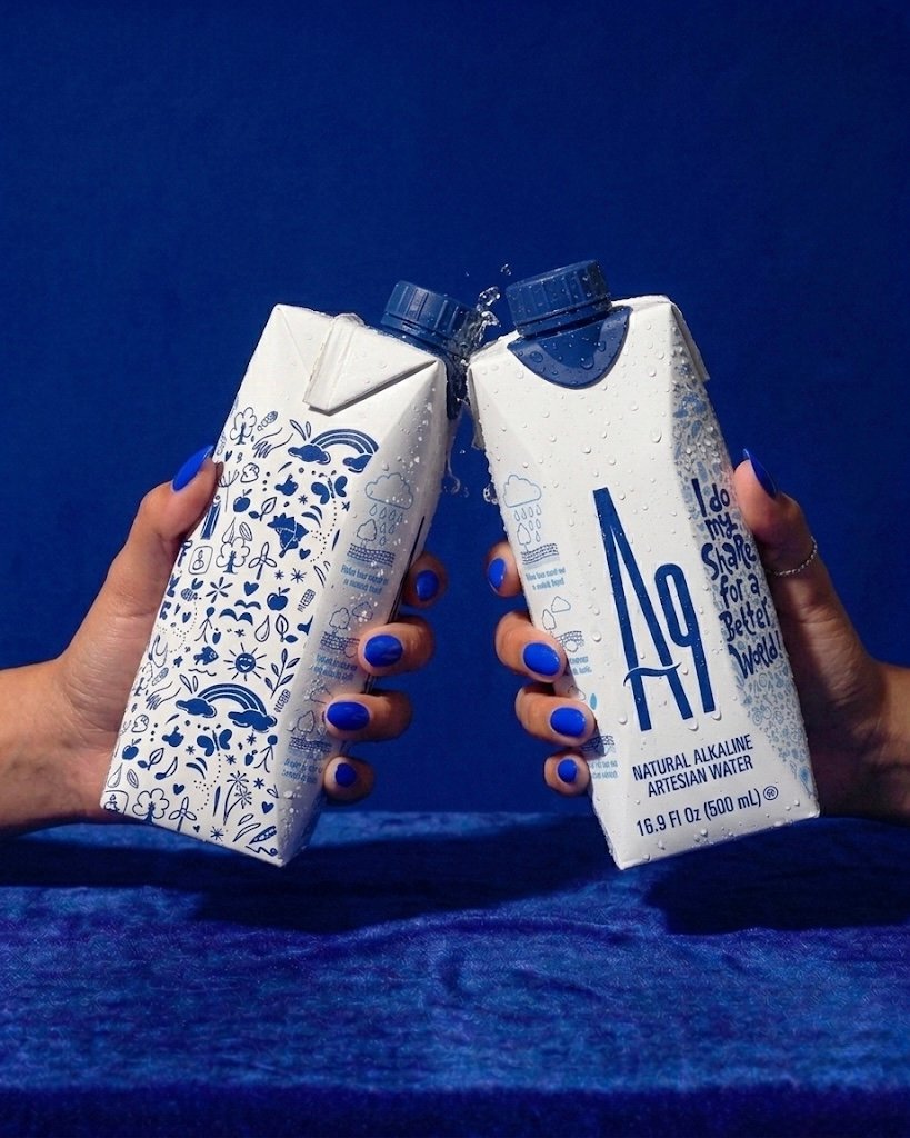Two people raising cold A9 natural alkaline water cartons against a deep blue background